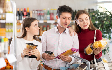 Happy teen girl with her parents deciding between packages of pasta in supermarket