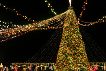 Brightly illuminated big Christmas tree decorated with garlands with shinig lights and ornaments at night, creating festive holiday atmosphere. Christmas and New Year holiday fair outdoor.
