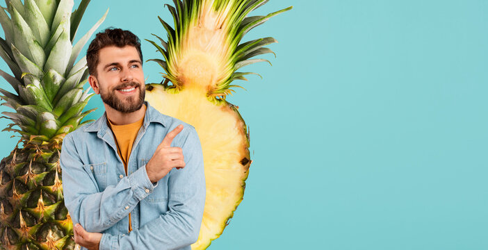 Smiling young man showcases an advertising banner on a blue background, pointing with confidence. His gesture highlights a special offer related to travel and diet, set against a pineapple backdrop.