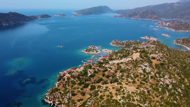 Drone footage captures the stunning aerial view of the historic Simena Castle and the picturesque Kalek&ouml;y village nestled on the coast of Kekova Island, Turkey. The turquoise waters of the Mediterrane
