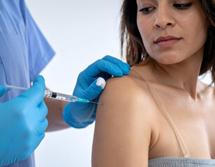 Healthcare worker administering an injection to a young woman's shoulder. Focus on medical procedure, vaccination, and patient care in a clinical setting.