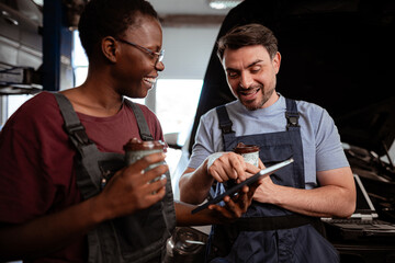 Mechanics sharing knowledge and enjoying drinks in a workshop at midday