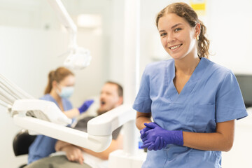 Obraz premium Woman dental assistant invites clients for professional dental hygiene and whitening. Qualified treatment in the dental studio