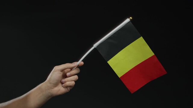 Hand holding belgium flag against black background, showcasing national pride in an isolated setting