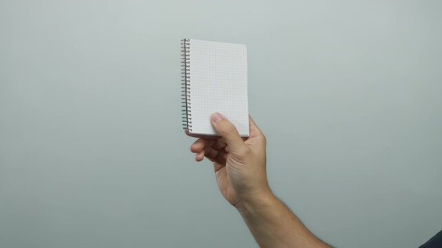 Man's hand holding a spiral notebook against a white isolated background, perfect for concepts of writing, planning, and note-taking.