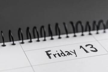 Close-up of a spiral notebook calendar displaying Friday 13, captured in grayscale to emphasize superstition, tension, and a moment of impending focus.