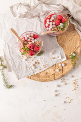 An overhead shot of two glasses of layered raspberry and chia seed pudding with fresh raspberries and white crowberry on a rustic wooden platter