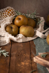 A rustic still life with russet apples in a string bag, evoking a cozy and autumnal mood on a dark wooden table