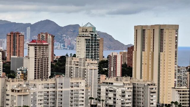 A panoramic view of a modern coastal city skyline set against a mountainous backdrop, showcasing urban architecture.
