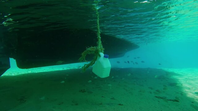 Fishing motorboat is parked in sandy shallow water school of Strongspine silver-biddy, Gerres longirostris swimming in its shadow on bright sunny day, underwater view