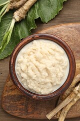 Tasty horseradish sauce and roots on wooden table, flat lay