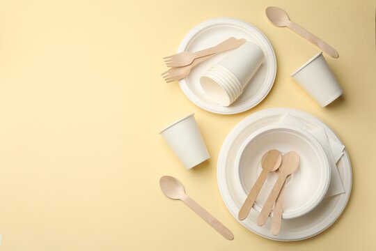 Set of disposable tableware on beige background, flat lay. Space for text