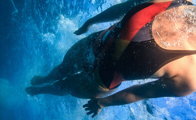 Professional swimmer moving fast in ocean water broght blue color on background, underwater shot