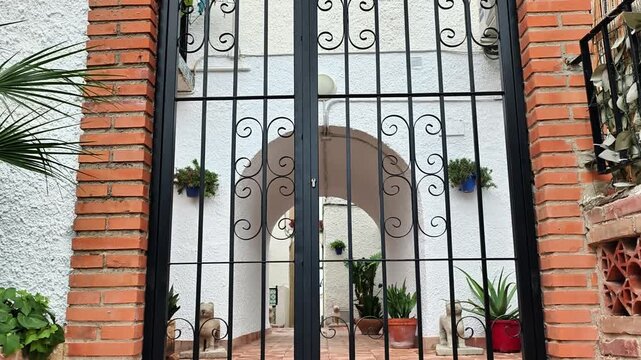 The video features a wrought iron gate framed by a weathered brick wall, leading to a serene space. Surrounding potted plants enhance the tranquil atmosphere