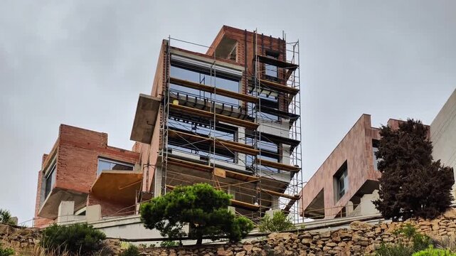 This video shows a large building being constructed on a hill, highlighting intricate scaffolding and bustling onsite activity against a scenic backdrop