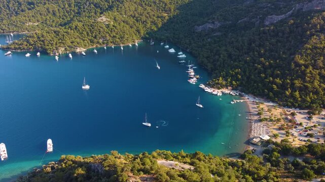 aerial perspective of Sarsala Koyu Sarsala Bay in Dalaman, Turkey, showcasing the tranquil turquoise waters of the Mediterranean, lush green hills, and numerous anchored yachts enjoying the serene coa