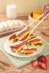 Fresh Breakfast Sandwich with Bacon and Egg Being Eaten with Chopsticks on Wooden Kitchen Table