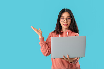 Naklejka premium Young female Asian programmer with laptop pointing at something on blue background