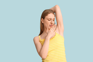 Fototapeta premium Young woman feeling smell of sweat on blue background. Concept of using deodorant