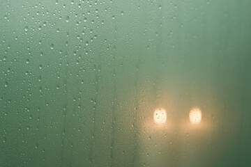 Foggy window with water droplets and blurred glowing lights creating soft, moody ambiance in humid indoor environment