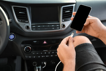 Man connecting white charging cable to mobile phone in car, closeup