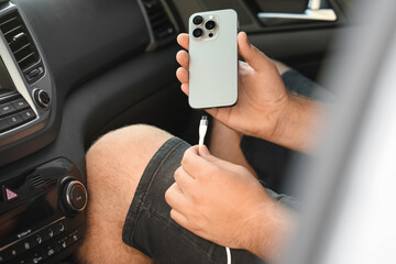 Man connecting white charging cable to mobile phone in car, closeup