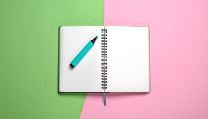 An open blank notebook with a spiral binding rests on a two-tone surface green and pink. A teal highlighter is placed on the page