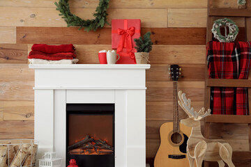 Cozy fireplace with stack of winter clothes, guitar and Christmas decorations near wooden wall