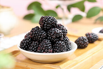 Fresh Black Yunnan Raspberries in White Bowl on Wooden Table with Green Leaves Background