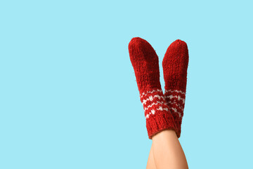 Legs of young woman in red knitted socks on blue background