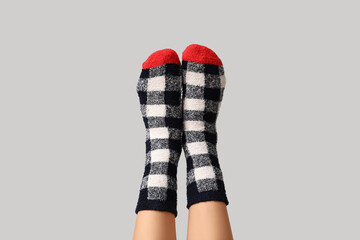 Legs of young woman in warm checkered socks on grey background