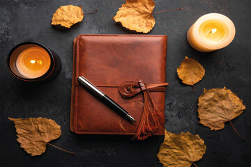 Stylish autumn flat lay featuring a brown leather journal, fountain pen, candles, and dried leaves with soft lighting.