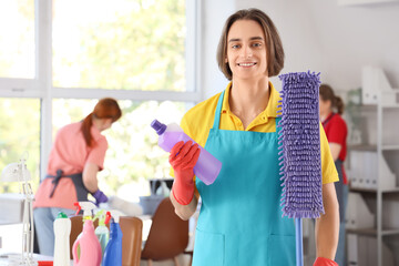 Male janitor with detergent and mop in office