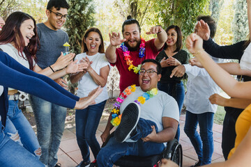 Group of Latin friends dancing at a party including a person in wheelchair, outdoors on a terrace in Mexico, Latin America. Hispanic men and women of different ages in social inclusion concept