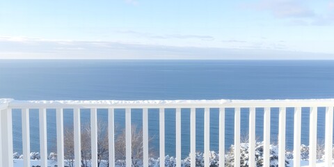 Snow covered white balcony railing overlooks a vast blue ocean under a clear pale sky