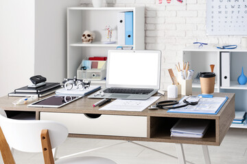 Medical student's workplace with blank laptop and ophthalmic trial frame in clinic