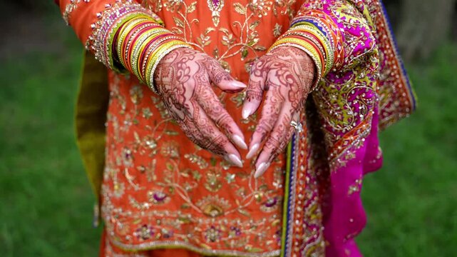 Close up view of Traditional Indian or Pakistan henna painted bridal hands with wedding rings. Colorful clothes, henna tattoo. Bride opens palms showing beautiful henna pattern 