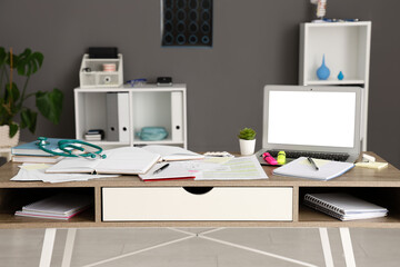 Medical student's workplace with blank laptop and notebooks in clinic