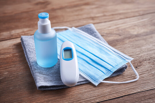 Medical face mask, thermometer and sanitizer on wooden background