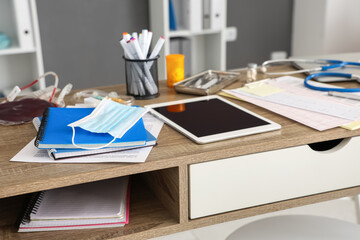 Medical mask with notebooks and tablet computer on student's table in clinic, closeup