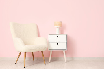 Soft armchair and table with lamp near pink wall in room