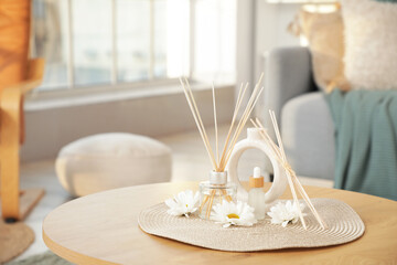 Reed diffuser with chrysanthemum flowers, essential oil and bamboo sticks on table in living room, closeup