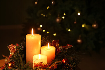 Composition with burning candles and Christmas wreath against decorated fir tree in evening