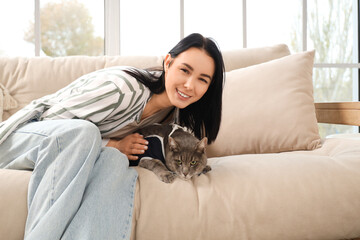 Young woman with her cat in recovery suit after sterilization on sofa at home