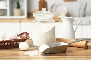 Flour in jar with rolling pin, scoop and eggs for preparing dough on kitchen counter
