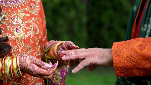 Bride is putting on the wedding ring on groom hand. Elements of Hindu bright wedding clothes. 