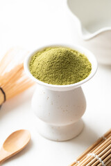 Matcha green tea powder with wooden spoon, bamboo whisk and Chawan bowl on white background