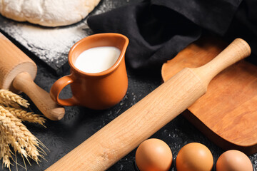 Composition with wooden rolling pin and ingredients for dough on black background, closeup