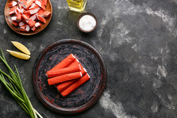 Plates with tasty crab sticks, pieces of lemon and green onion on black background © Pixel-Shot
