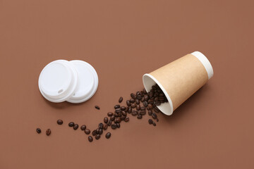 Overturned disposable cup with scattered coffee beans on brown background